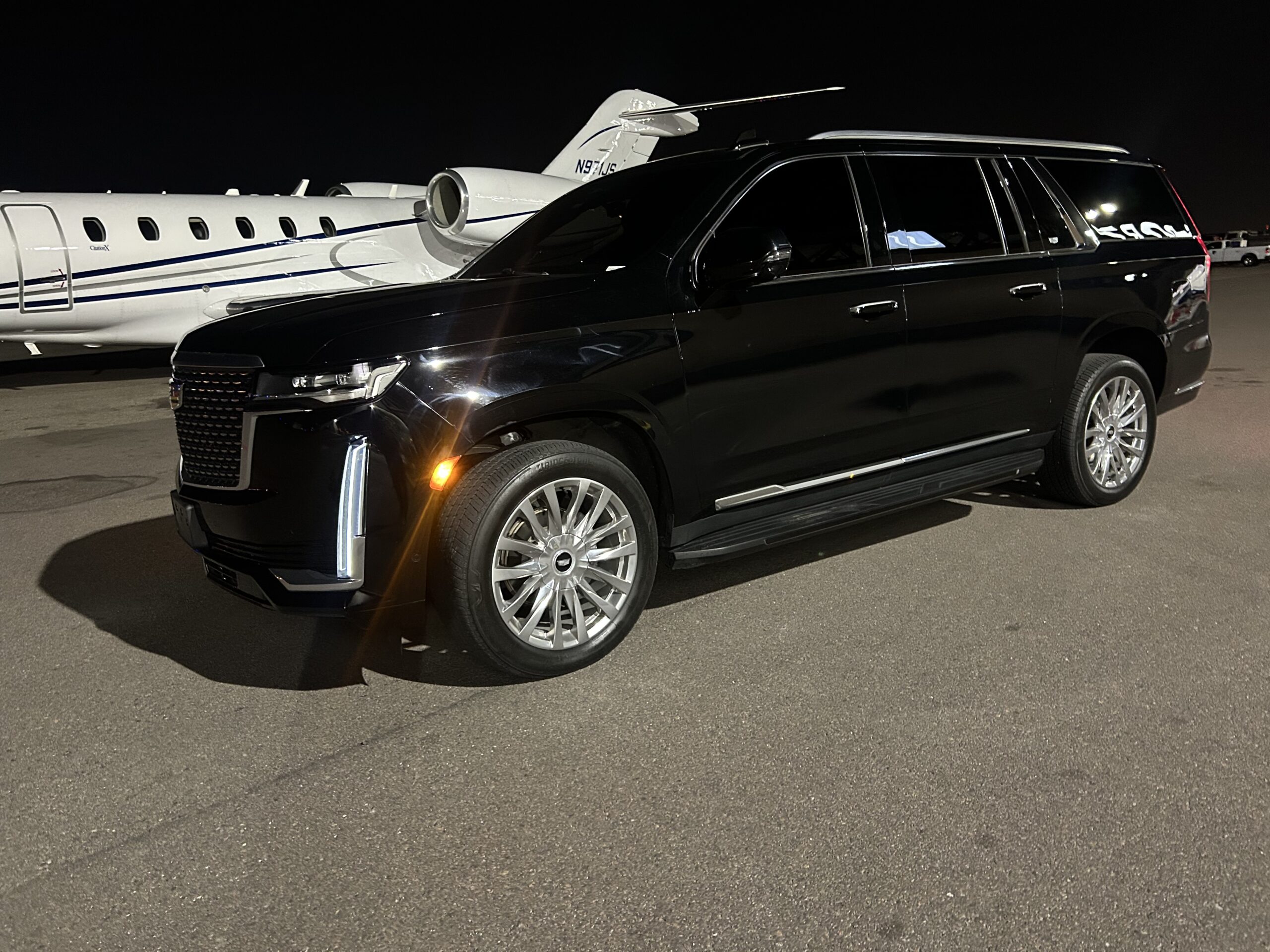 A sleek Cadillac Escalade is prominently featured with a polished private jet serving as its dramatic backdrop